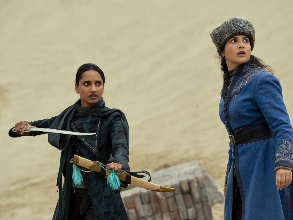 Two women look to the side, one wielding a sword.