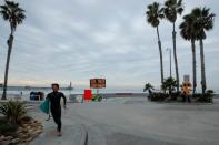 A surfer passes a warning sign on the beach as new stay-at-home orders begin in Southern California