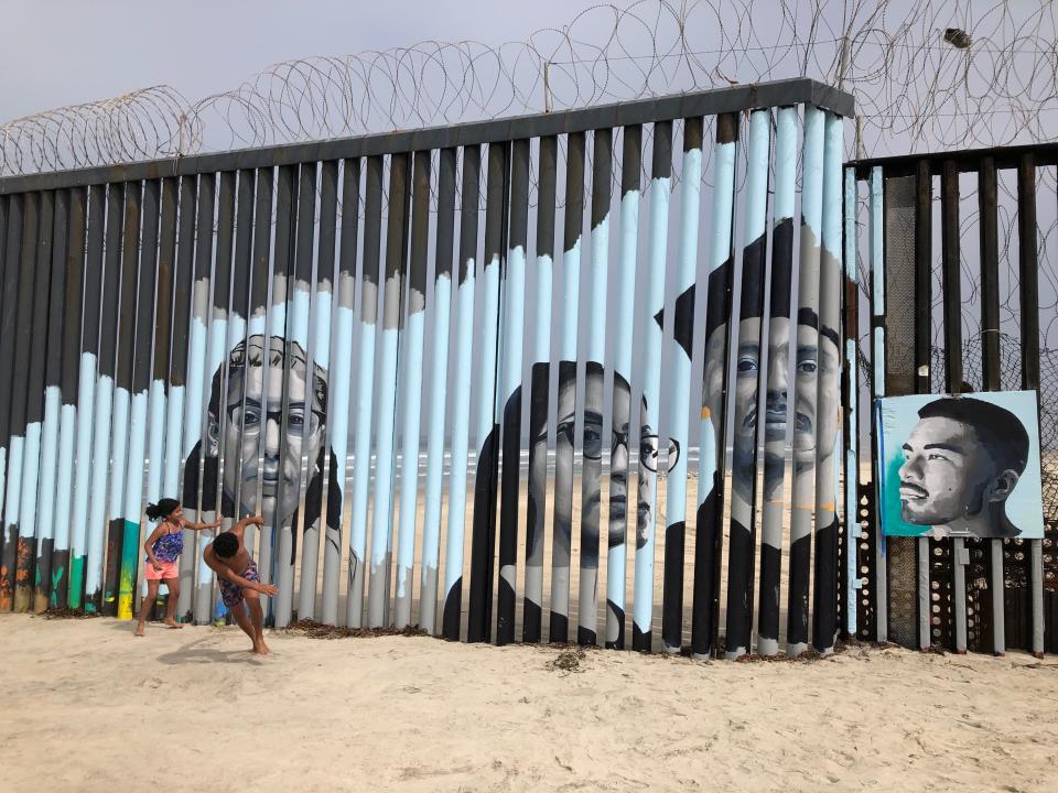 Children play in front of a new mural on the Mexican side of a border wall in Tijuana, Mexico Friday, Aug. 9, 2019. The mural shows faces of people deported from the U.S. with barcodes that activate first-person narratives on visitors' phones. Lizbeth De La Cruz Santana conceived the interactive mural in Tijuana as part of doctoral dissertation at the University of California, Davis. (AP Photo/Elliot Spagat)