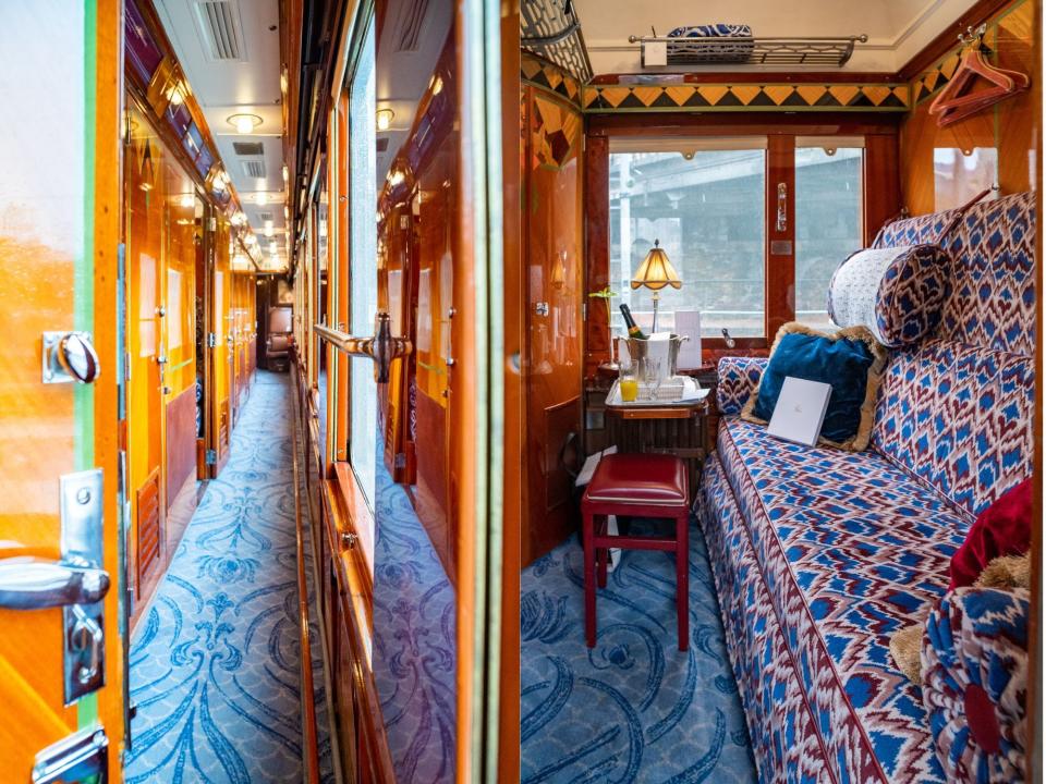 The inside of a train with wooden interiors shows a narrow corridor and a train cabin with wood finishings and a plush red and blue couch.