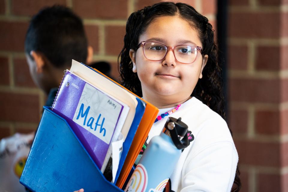 Ashley Soto, a third grader at Cora Kelly School, holds a bin with her folders and water bottle before entering class in Alexandria, Va.