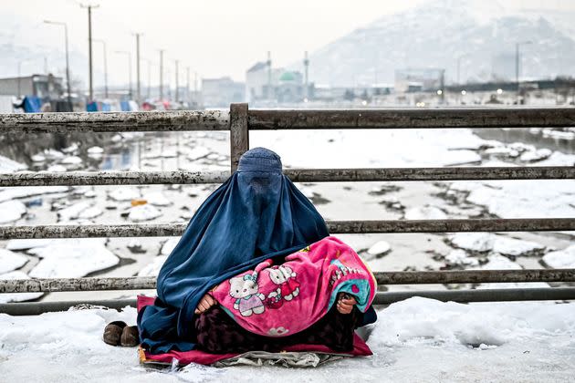 A burqa-clad Afghan woman sits with a child on her lap as she seeks alms from passersby on a bridge covered with snow in Kabul on Thursday. (Photo: Mohd Rasfan/AFP/Getty Images)