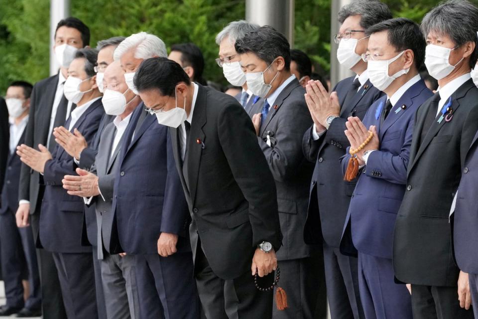 Japan’s prime minister Fumio Kishida, alongside officials and employees, offers prayers as the funeral procession passes (Reuters)
