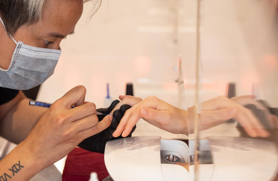 A nail technician at work behind a plastic protective as they reopen to customers on following the easing of lockdown restrictions in England.(Getty)