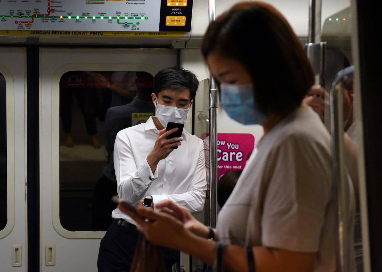 Commuters wearing face masks as a preventive measure against COVID-19 look at their mobile phones on the MRT on 18 March, 2020. (PHOTO: AFP via Getty Images)