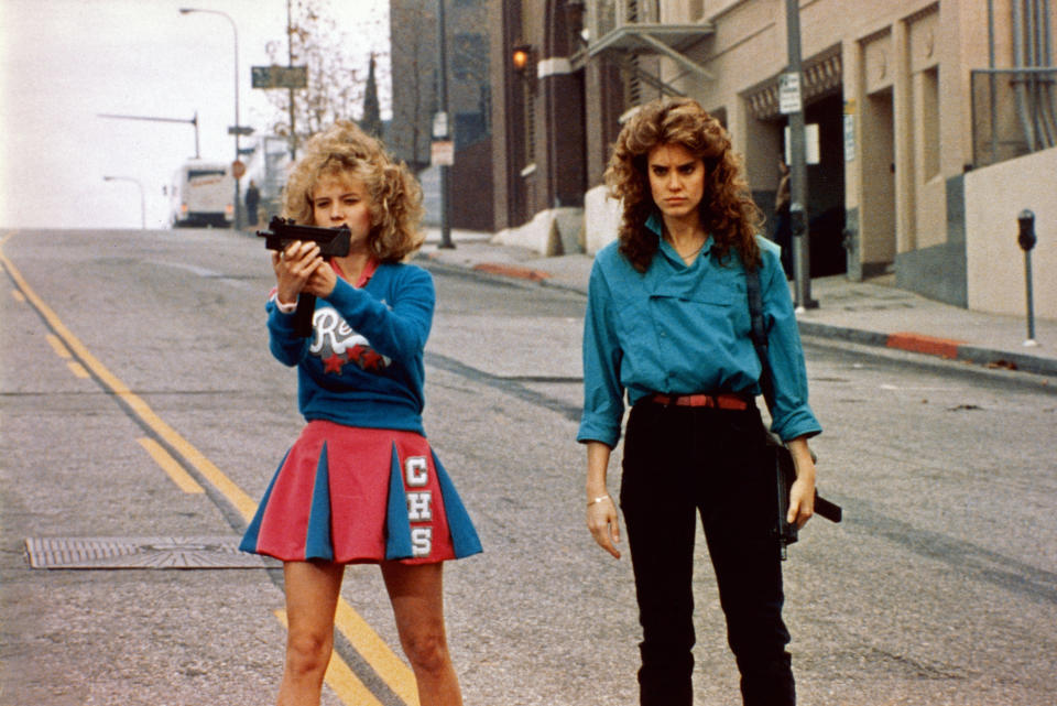 Two teenage girls hold machine guns in an empty city street