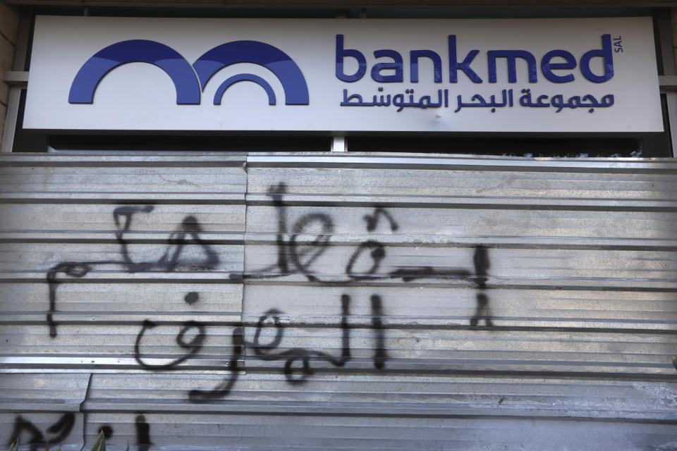 A door of a closed bank is spray painted with a message in Arabic that reads, "Down with the rule of the banks," in Beirut, Lebanon, Tuesday, Nov. 12, 2019. Lebanon's banking association says banks will stay closed due to a strike by employees, as country's financial crisis worsens. (AP Photo/Hassan Ammar)