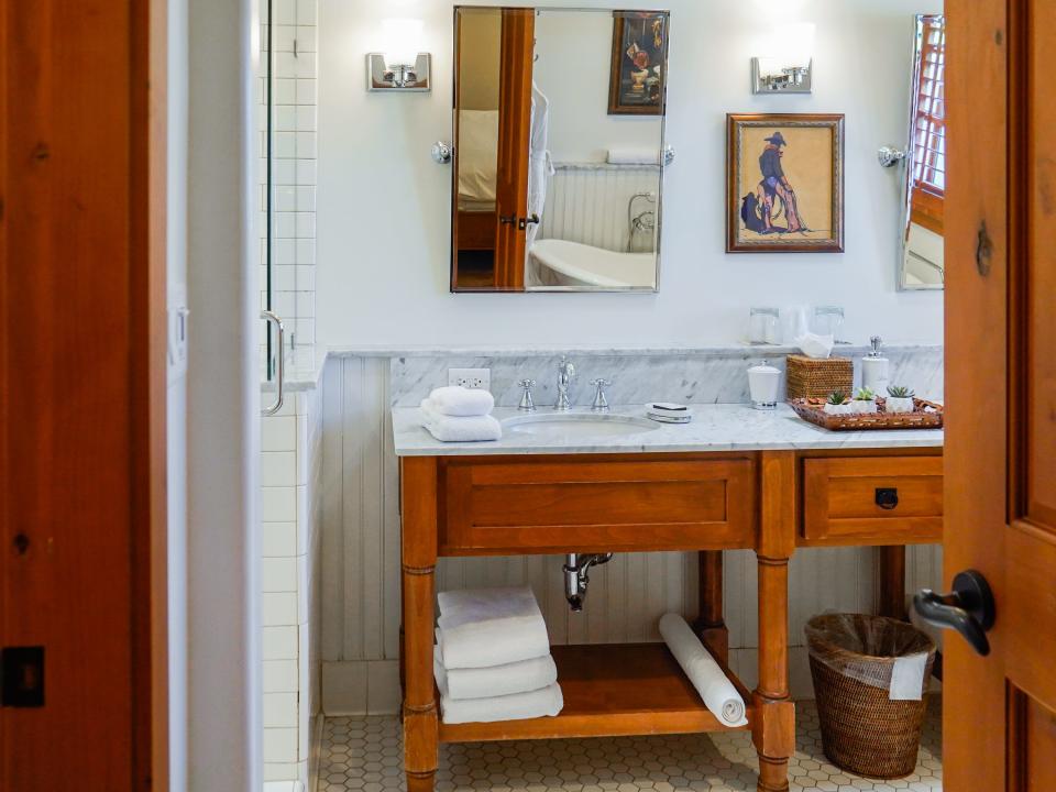 A white bathroom with a a wooden vanity with a marble countertop and sink