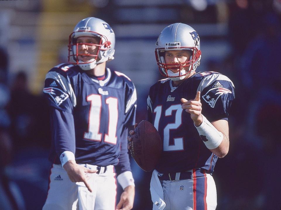 Tom Brady points and holds a football while standing next to Drew Bledsoe in 2001.