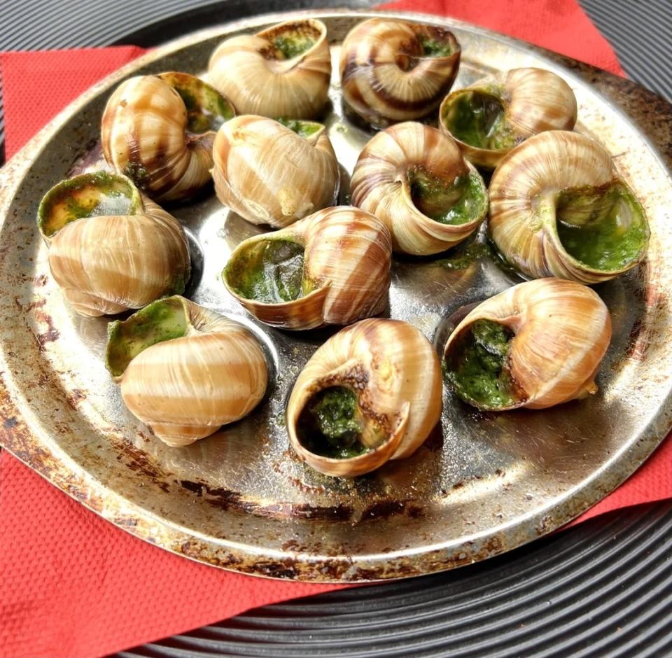 Escargot dish on a metal platter, garnished with herbs and served on red napkins