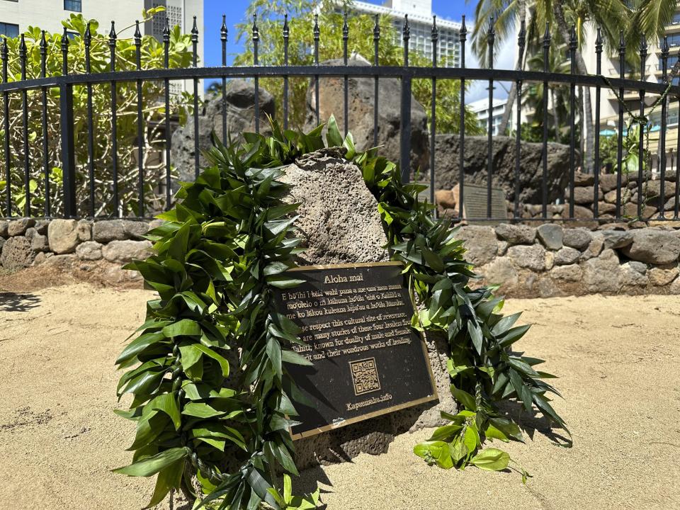 Lei are draped on a plaque in front of the Kapaemahu stones in Honolulu on Tuesday, Oct. 24, 2023. Honolulu officials on Tuesday introduced a new interpretive plaque for four large boulders in the center of Waikiki that honor Taihitian healers of dual male and female spirit who visited Oahu some 500 years ago. (AP Photo/Audrey McAvoy)