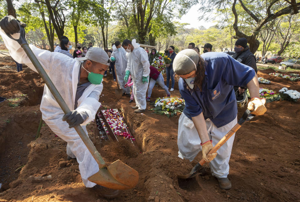 Cemetery workers bury 65-year-old Maria Joana Nascimento, whose family members, behind, suspect died of COVID-19, at Vila Formosa cemetery in Sao Paulo, Brazil, Thursday, Aug. 6, 2020. Brazil is nearing 3 million cases of COVID-19 and 100,000 deaths. (AP Photo/Andre Penner)