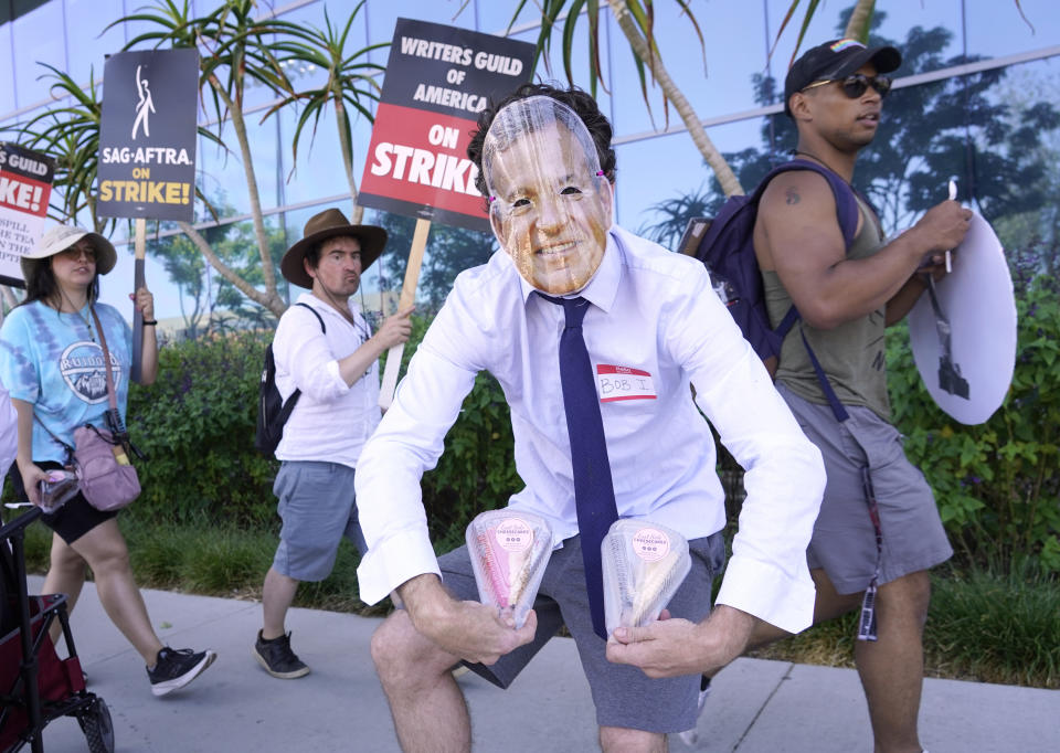 SAG-AFTRA member Gregory Lay, owner of the store East Side Cheesecakes, dresses as Disney CEO Bob Iger as he hands out slices of cake to picketers outside Netflix studios on Tuesday, July 18, 2023, in Los Angeles. The actors strike comes more than two months after screenwriters began striking in their bid to get better pay and working conditions and have clear guidelines around the use of AI in film and television productions. (AP Photo/Chris Pizzello)