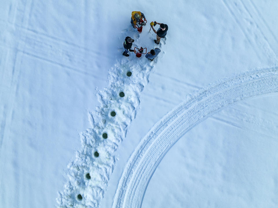 This photo provided by Aroostook UAS shows volunteers creating a giant ice carousel on a frozen lake drill holes to serve as a guide for the path cut through the ice, on Wednesday, March 29, on Long Lake in Madawaska, Maine. (Aroostook UAS via AP)