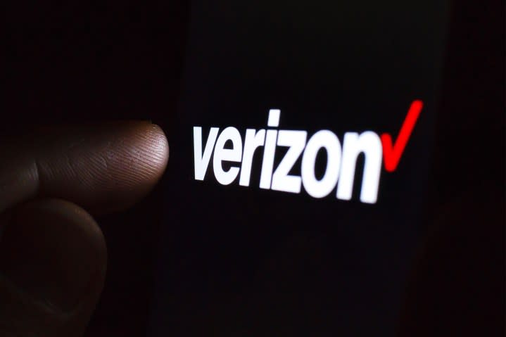 Logo Verizon sur l'écran d'un smartphone dans une pièce sombre et un doigt le touchant.