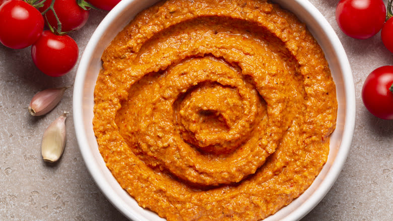 Bowl of romesco sauce with tomatoes in the background