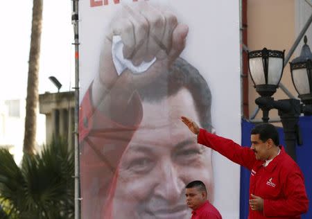 Venezuela's President Nicolas Maduro (R) gestures in front of a giant image of Venezuela's late President Hugo Chavez, during a meeting with workers of the Venezuelan state oil company PDVSA, outside Miraflores Palace in Caracas January 12, 2016. REUTERS/Carlos Garcia Rawlins