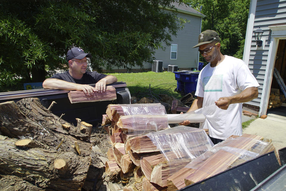 Alton Lucas, right, wraps firewood for sale as he and neighbor Ryan Isaac, a correctional officer, chat outside Lucas' home outside of Raleigh, N.C., on Friday, June 18, 2021. “I started the landscaping company, to be honest with you, because nobody would hire me because I have a felony,” said Lucas, whose business got off the ground with the help of Inmates to Entrepreneurs, a national nonprofit assisting people with criminal backgrounds by providing practical entrepreneurship education. (AP Photo/Allen G. Breed)