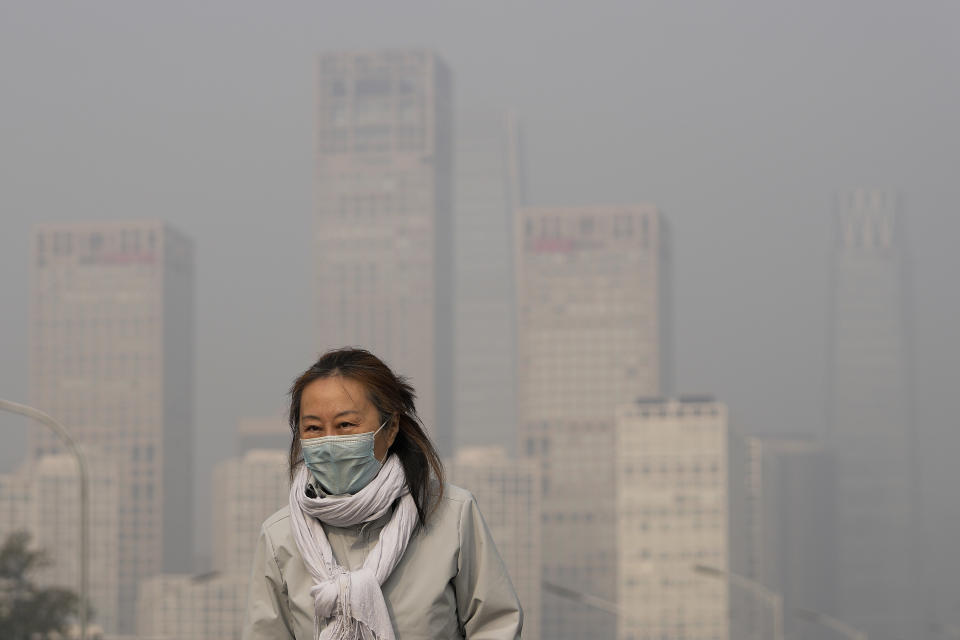 FILE - A woman wearing a face mask to protect from COVID-19 walks against the office buildings in Central Business District shrouded by pollution haze in Beijing, Thursday, Nov. 18, 2021. The U.N. health agency said Monday, April 4, 2022, nearly everybody in the world breathes air that doesn’t meet its standards for air quality, calling for more action to reduce fossil-fuel use, which generates pollutants that cause respiratory and blood-flow problems and lead to millions of preventable deaths each year. (AP Photo/Andy Wong, File)