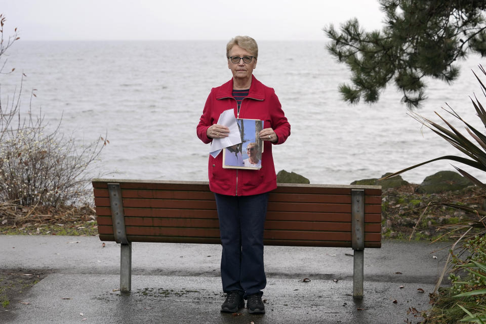 Diane Ostrander poses for a photo, Thursday, Jan. 20, 2022, in Kirkland Wash., while holding a picture of her and her son, who is now in a behavioral health hospital, during happier times together. For months, Ostrander worried desperately about her son as he faced a mental-health crisis, but the police Ostrander begged for help relayed a consistent message: A new state law meant officers couldn't take her son to get help against his will, even though mental health professionals and a judge ordered it. The park bench behind her on the Lake Washington waterfront was one fo the last places Ostrander said she and her son were able to spend peaceful time together. (AP Photo/Ted S. Warren)