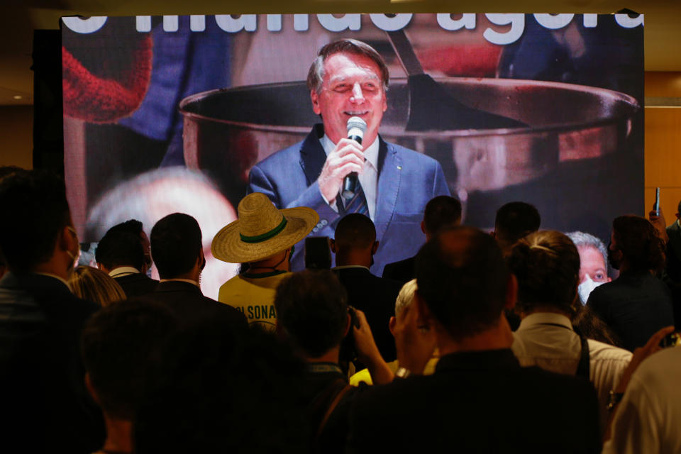 Supporters watch on a screen, Brazilian President Jair Bolsonaro speaking during a ceremony where he officially joined the centrist Liberal Party, in Brasilia, Brazil, Tuesday, Nov. 30, 2021. (AP Photo/Raul Spinasse)