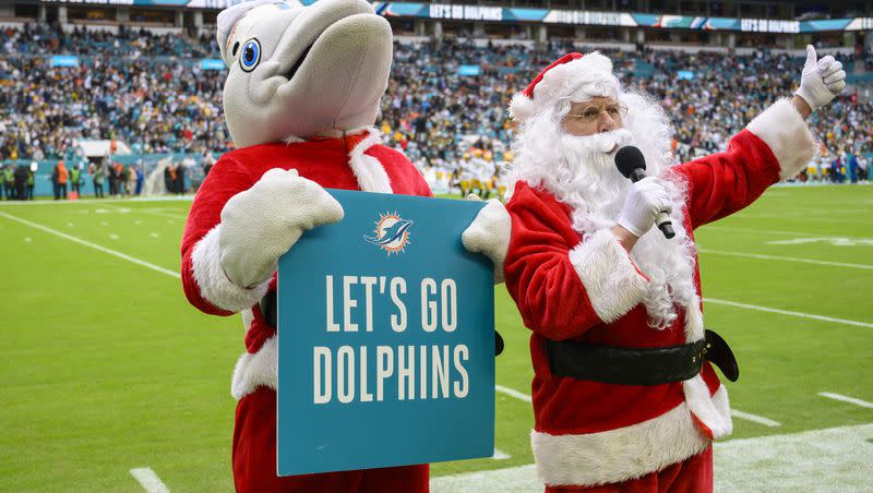 Miami Dolphins mascot T.D., wearing a Santa jacket and sign, helps Santa cheer on the fans before an NFL football game against the Green Bay Packers, Sunday, Dec. 25, 2022, in Miami Gardens, Fla.
