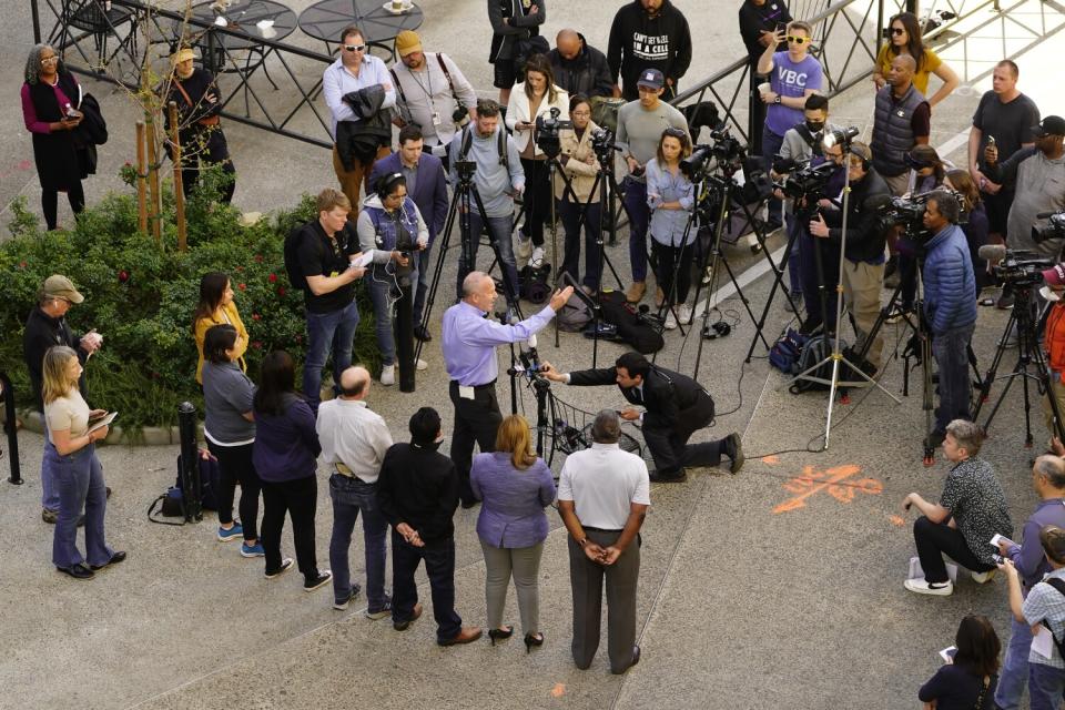 A man standing in front of video cameras speaks to journalists