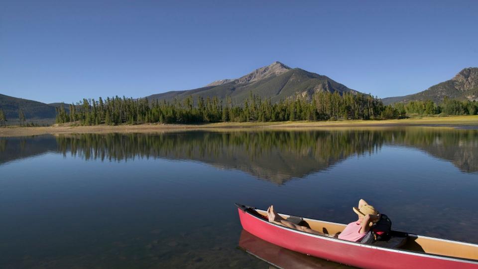 A woman relaxeson a boat on a calm lake under clear blue sky