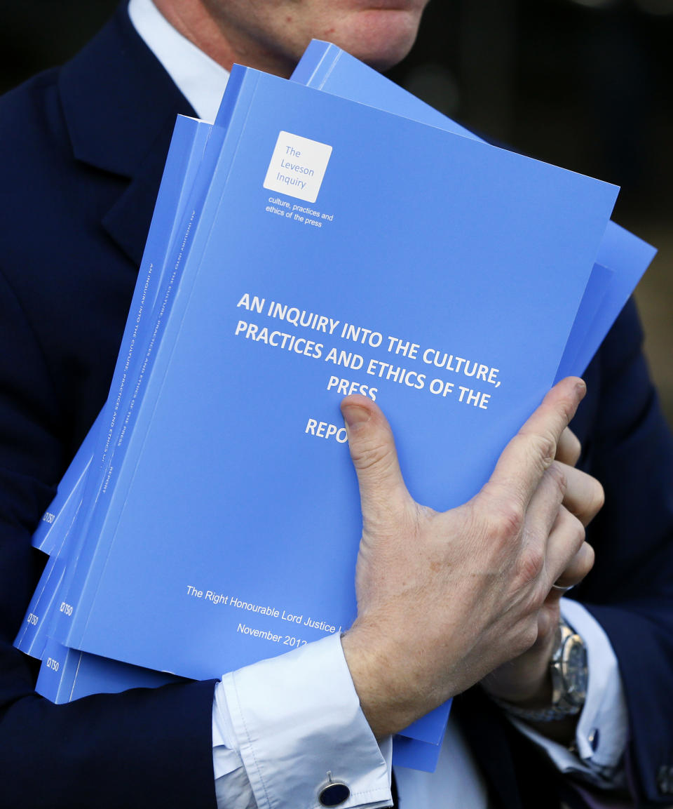 A man carries copies of the Leveson Inquiry report as he leaves the Queen Elizabeth II Conference Centre where Lord Justice Brian Leveson released his report, after a year long inquiry, into the culture and practices of the British press and his recommendations for future regulation to prevent phone hacking, data theft, bribery and other abuses, London, Thursday, Nov. 29, 2012. (AP Photo/Kirsty Wigglesworth)