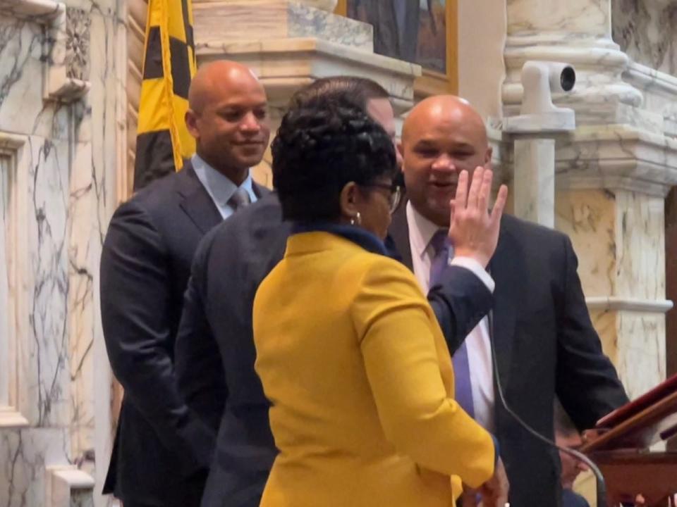 Maryland Senate President Bill Ferguson, hand up, swears in State Treasurer Dereck Davis in Annapolis on Feb. 21, 2023. Governor Wes Moore, left, and House Speaker Adrienne Jones, in yellow, look on in the House chamber.