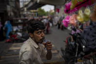 A roadside cotton candy vendor drinks water from a plastic pouch as he waits for customers at a weekly market in New Delhi, India, Wednesday, June 29, 2022. India banned some single-use or disposable plastic products Friday as a part of a longer federal plan to phase out the ubiquitous material in the nation of nearly 1.4 billion people. (AP Photo/Altaf Qadri)