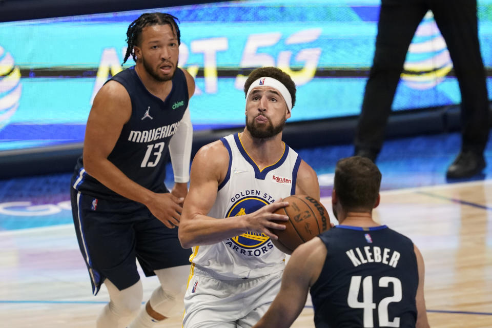 Golden State Warriors guard Klay Thompson, center, drives to the basket between Dallas Mavericks guard Jalen Brunson (13) and forward Maxi Kleber (42) during the second half of Game 3 of the NBA basketball playoffs Western Conference finals, Sunday, May 22, 2022, in Dallas. (AP Photo/Tony Gutierrez)