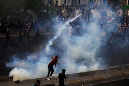 Demonstrator throws a tear gas canister used by Iraqi security forces as others disperse during a protest over unemployment, corruption and poor public services, in Baghdad