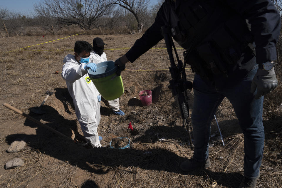 A National Guardsman hands a bucket to a forensic technician during an excavation on a plot of land referred to as a cartel "extermination site" where burned human remains are buried, on the outskirts of Nuevo Laredo, Mexico, Tuesday, Feb. 8, 2022. The official total of Mexico’s missing is nearly 100,000. Even without the civil wars or military dictatorships that afflicted other Latin American countries, Mexico’s disappeared are exceeded in the region only by war-torn Colombia. (AP Photo/Marco Ugarte)