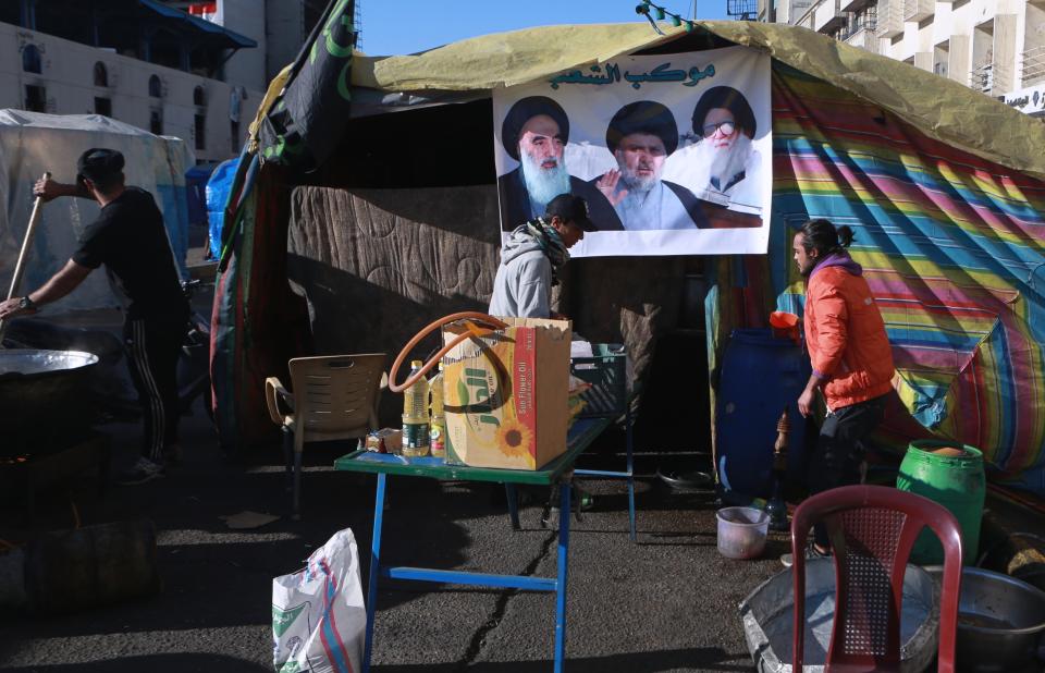 Free food is prepared for protesters during the ongoing anti-government protests next to a poster of Muqtada al-Sadr whose image is centered between the image of his father, Ayatollah Mohammed Sadiq al-Sadr, right, and Shiite spiritual leader Grand Ayatollah Ali al-Sistani, left, in Tahrir Square in Baghdad, Iraq, Saturday, Feb. 1, 2020. Influential and radical cleric Muqtada al-Sadr called for his followers to return to the street, one week after he withdrew support for anti-government demonstrators camped out in Baghdad's Tahrir Square. (AP Photo/Khalid Mohammed)