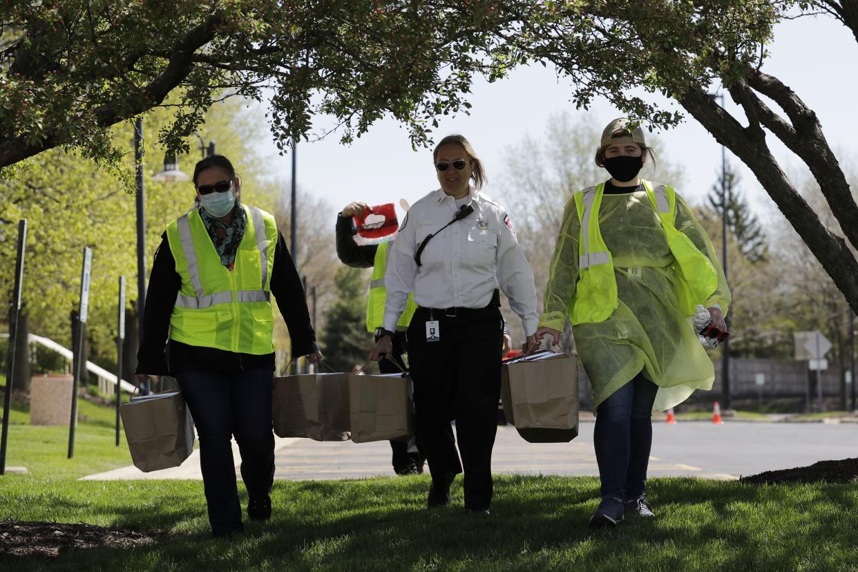 Staff members of The Village of Schaumburg and a firefighter carry masks to the parking lot of Boomers Stadium in Schaumburg, Ill. on Wednesday, May 6, 2020. The Village of Schaumburg distributed 70,000 masks to residents of the northwest suburb as the coronavirus pandemic continues. The distribution event is from Wednesday, May 6, through Friday, May 8, by age and last name from 10 a.m. to 3 p.m.