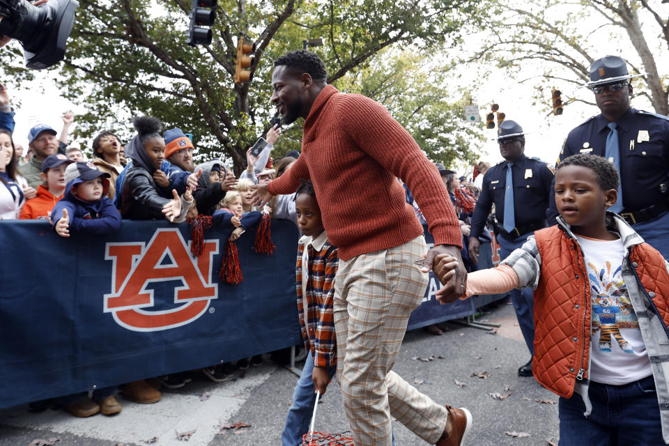 Auburn interim head coach Carnell Williams waves to fans as he participates in the Tiger Walk with his sons, Cuinn, left, and Cole, right, before an NCAA college football game Saturday, Nov. 19, 2022, in Auburn, Ala. (AP Photo/Butch Dill)