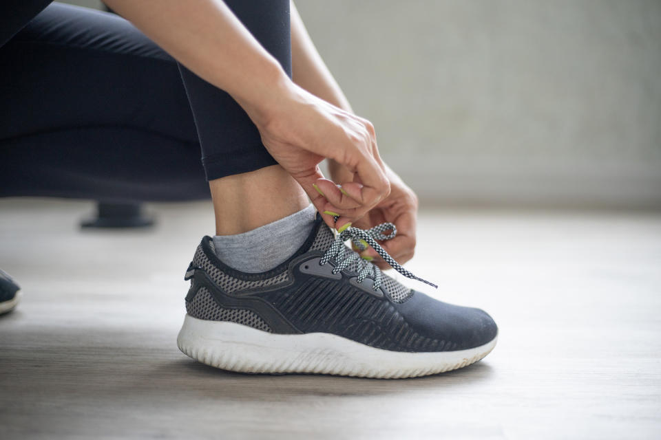 A person tying their gray sneaker