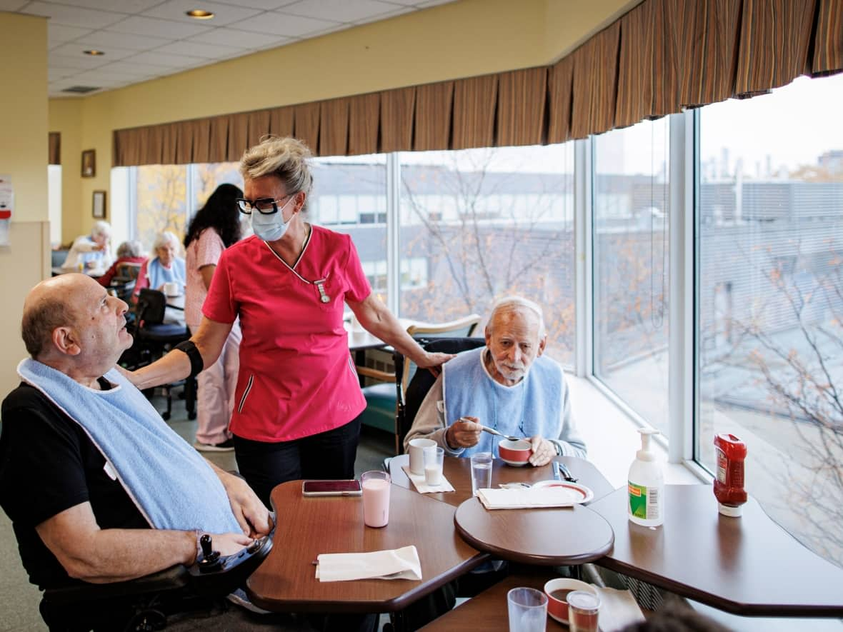 A personal support worker chats with Louis Capozzi, left, and James Armstrong in the dining room at Lakeshore Lodge, a City of Toronto-run long term care home, on Oct. 26, 2022. (Evan Mitsui/CBC - image credit)