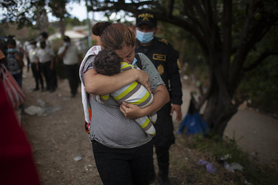 A woman carries her son as Honduran migrants confront Guatemalan soldiers and police manning a roadblock that prevents them from advancing toward the US, on the highway in Vado Hondo, Guatemala, Monday, Jan. 18, 2021. The roadblock was strategically placed at a chokepoint on the two-lane highway flanked by a tall mountainside and a wall leaving the migrants with few options. (AP Photo/Sandra Sebastian)