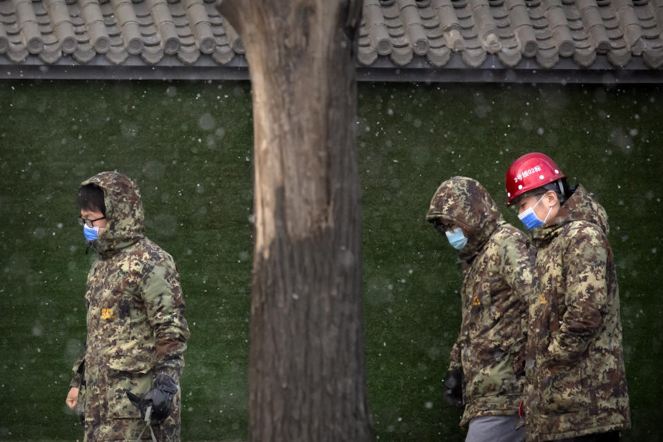 Construction workers wearing face masks to protect against the spread of the coronavirus walk along a street during a snowy morning in Beijing, Tuesday, Jan. 19, 2021. A Chinese province near Beijing grappling with a spike in coronavirus cases is reinstating tight restrictions on weddings, funerals and other family gatherings, threatening violators with criminal charges. (AP Photo/Mark Schiefelbein)