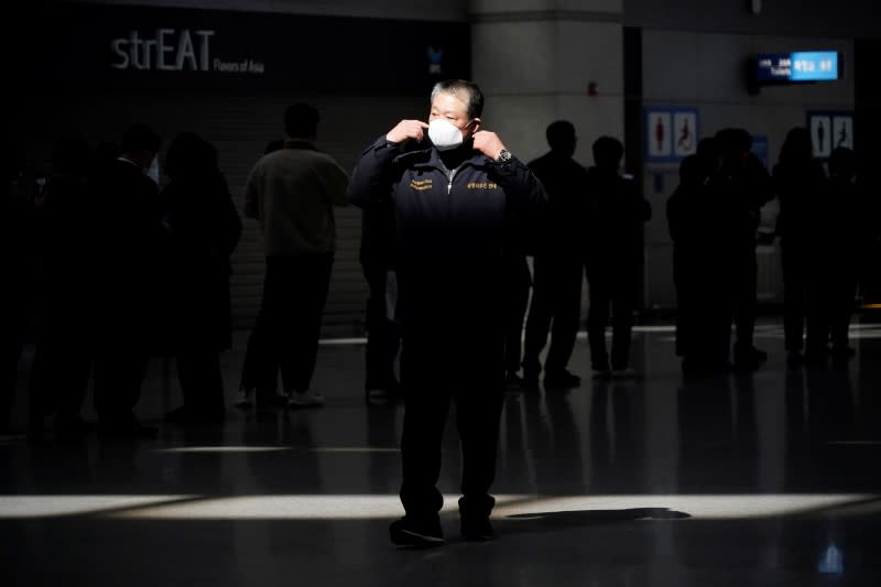 A man wearing a mask to prevent contracting the coronavirus walks past people waiting in a line to buy masks at Incheon International Airport in Incheon