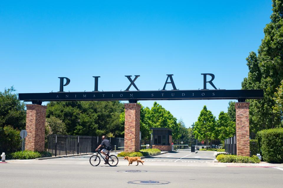 A man rides his bicycle and walks his dog past the entry gates at the headquarters of Pixar Animation Studios in downtown Emeryville, California, with logo visible, June 12, 2018. (Photo by Smith Collection/Gado/Getty Images)