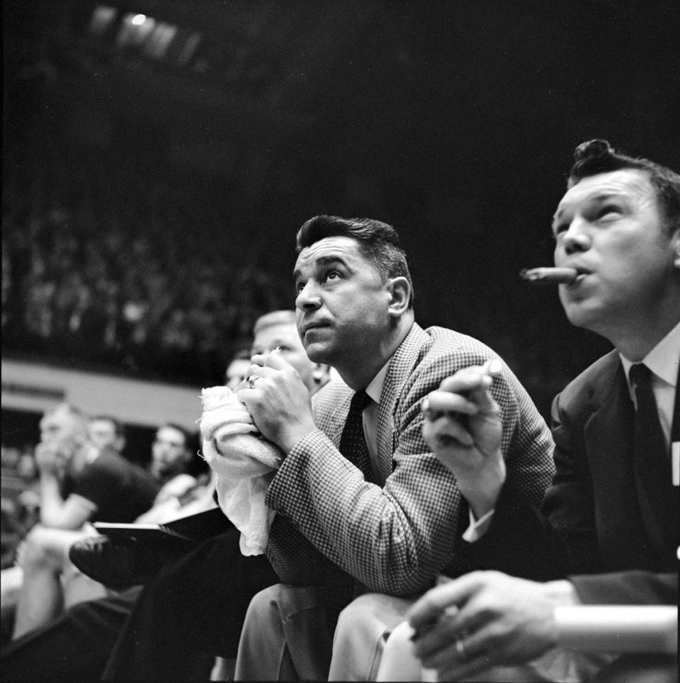 An assistant coach lights up a cigar on the bench (right) as Clemson coach Press Maravich works his trademark towel during a game in the 1957 ACC Tournament in Reynolds Coliseum.