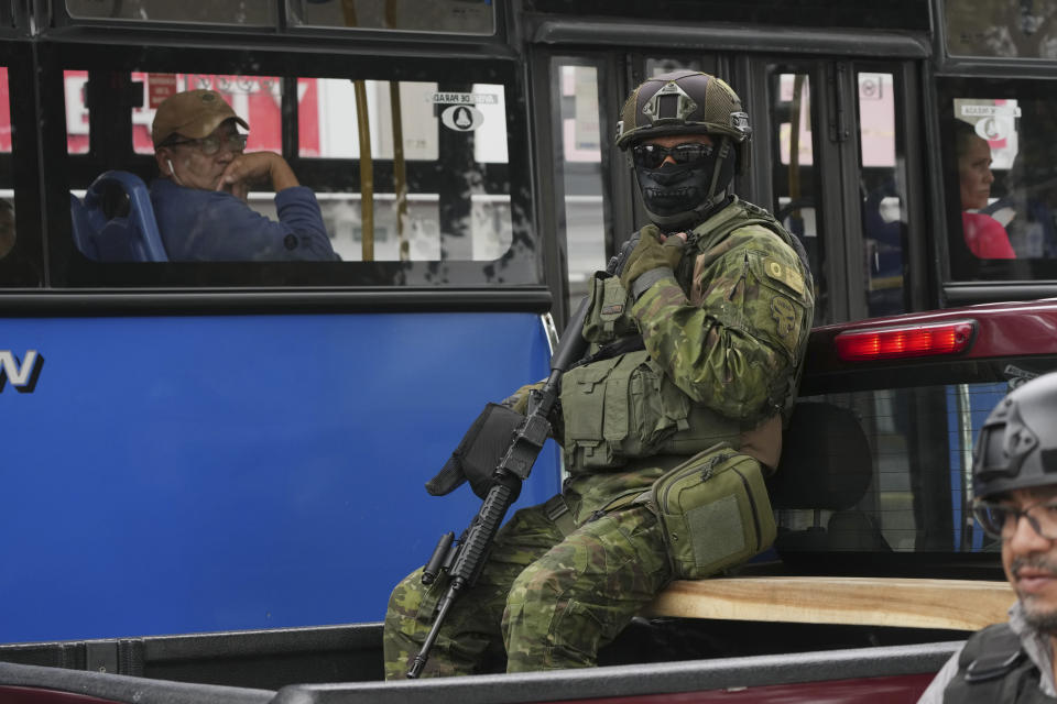 Un soldado se sienta en la parte trasera de un camión mientras patrulla frente a un autobús de cercanías en el norte de Quito, Ecuador, el jueves 11 de enero de 2024. El presidente Daniel Noboa decretó el lunes un estado de emergencia nacional debido a una ola de criminalidad, una medida que permite las autoridades suspender derechos ciudadanos y movilizan al ejército. (Foto AP/Dolores Ochoa)