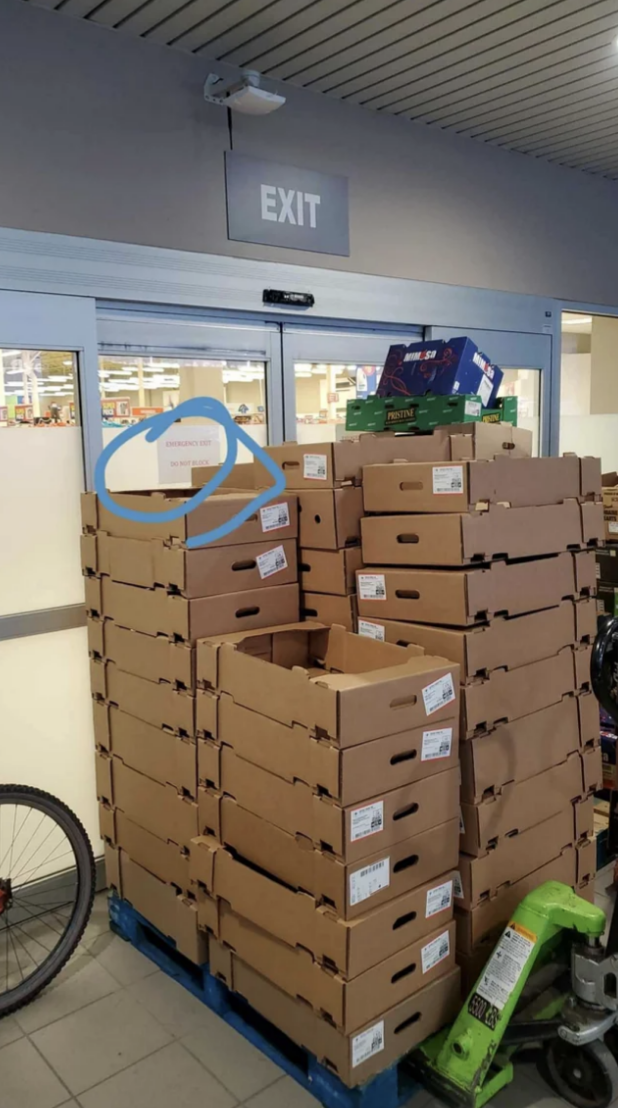 Stacks of cardboard crates in front of a door with a "Do not block" sign