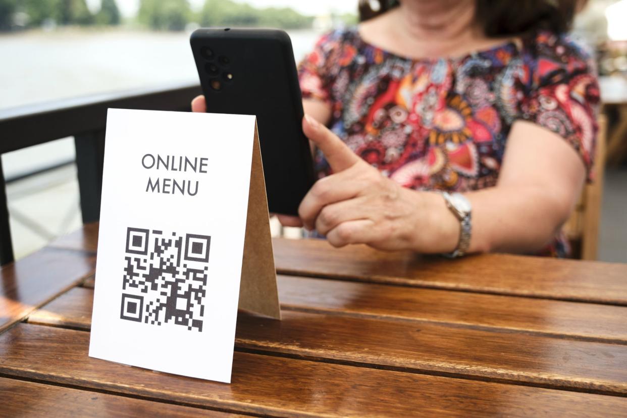 Mature unrecognizable woman scanning a QR code to access a restaurant menu; use of contactless technology in everyday life.