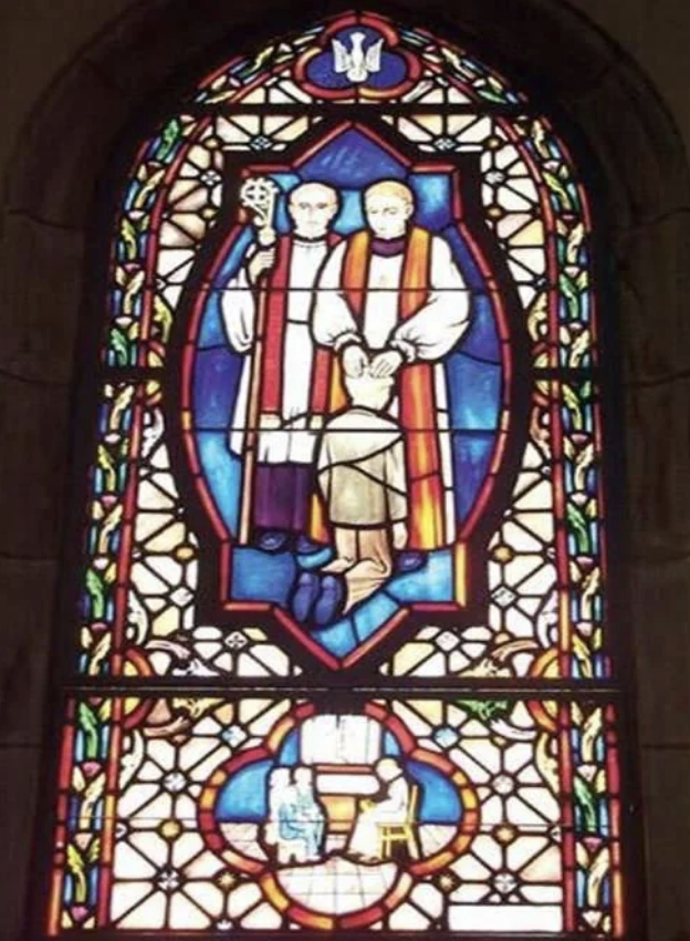 A stained glass window depicting two religious figures holding a child, surrounded by intricate patterns