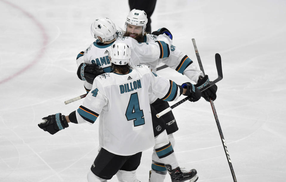 San Jose Sharks' Brent Burns, back, hugs Dylan Gambrell as teammate Brenden Dillon (4) joins the celebration after Gambrell scores a goal against the Minnesota Wild in the third period of an NHL hockey game, Saturday, Feb. 15, 2020, in St. Paul, Minn. San Jose won 2-0.(AP Photo/Tom Olmscheid)