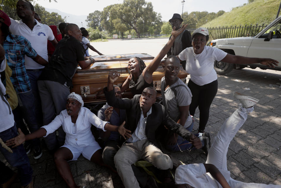 Mourners and demonstrators who were carrying the coffins with the remains of two victims of the ongoing violence take shelter around the coffins after clashes erupted between demonstrators and the Presidential Guard, near the Presidential Palace in Port-au-Prince, Haiti, Wednesday, Oct. 16, 2019. At last two people were injured in the clashes the while thousands across Haiti attended funerals for protesters who have died in ongoing demonstrations aimed at ousting President Jovenel Moise. (AP Photo/Rebecca Blackwell)